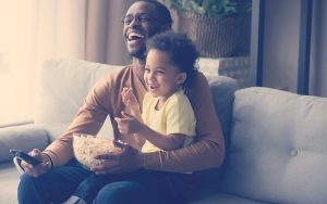 Papa e hijos comiendo palomitas y viendo una películas para papás