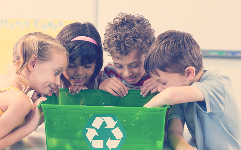 Niños reciclando en una caneca verde