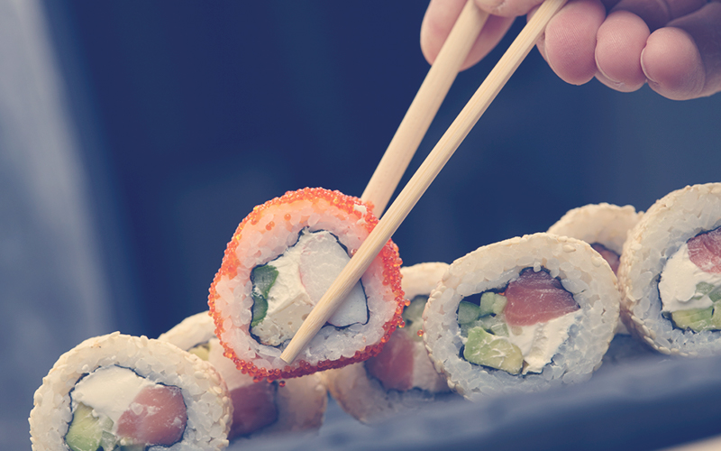 persona utilizando palitos chinos para comer sushi