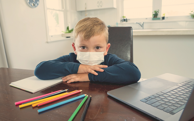 Niño en cuarentena con tapabocas estudiando en su casa