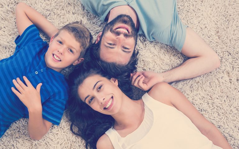 Familia sonríe mientras están acostados en la alfombra