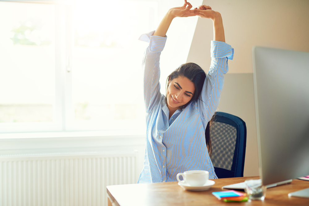 Mujer estirándose en su puesto de trabajo.