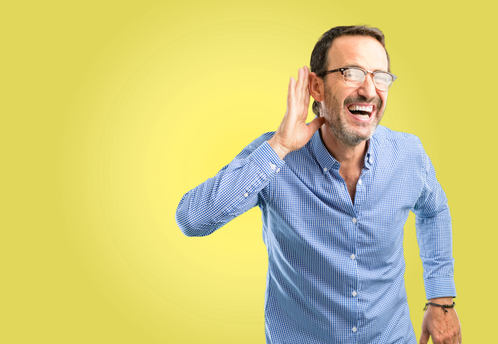 Un hombre guapo de mediana edad que está cerca del oído tratando de escuchar noticias interesantes que expresan concepto de comunicación y chismes