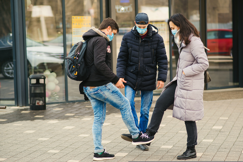 Personas saludándose con el pie mientras usan mascarillas 