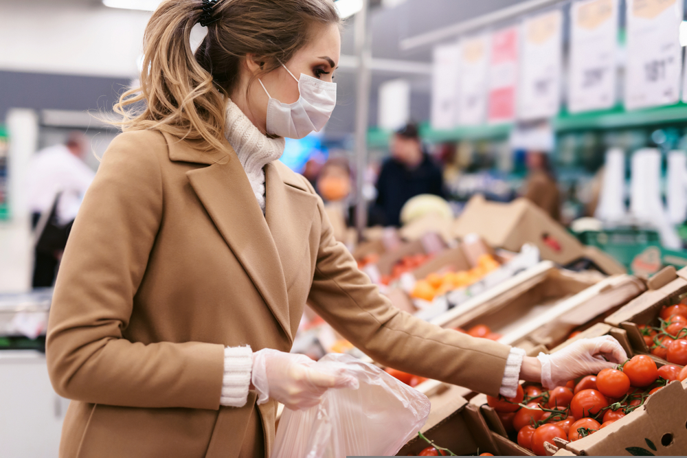  Una joven compra tomates en un supermercado. Mujer con mascarilla facial y guantes para prevenir la infección.