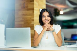 Mujer emprendedora onriendo al lado de un computador portátil