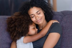 Mama e hija abrazándose sentadas en un sofá