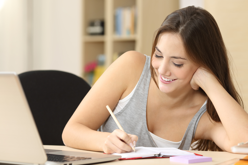 Estudiante feliz tomando notas en una agenda sentada en un escritorio en casa
