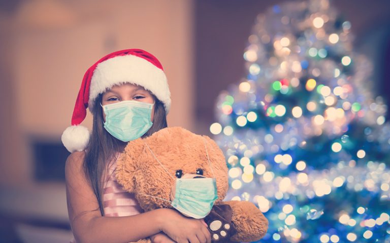 Niña con osito de peluche con máscara, coronavirus de Navidad y concepto de pandemia