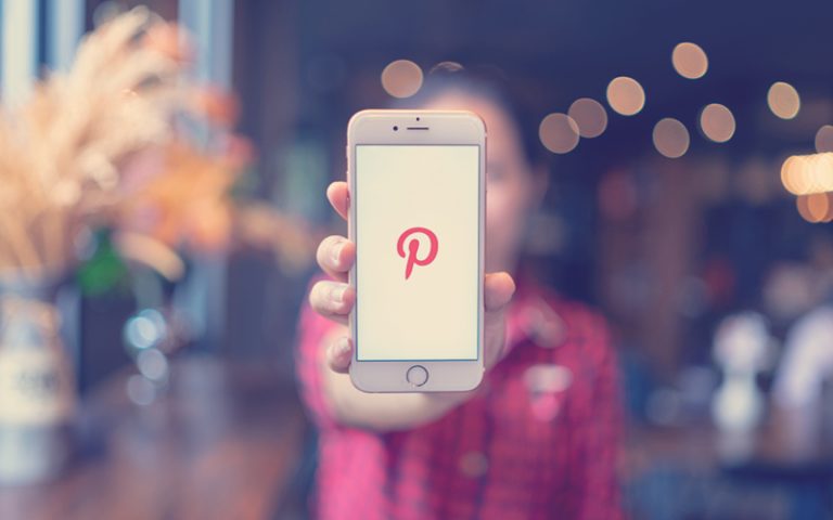 Mujer con un celular que muestra el logo de Pinterest