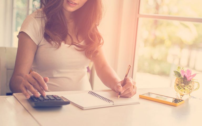 Una mujer que usa la calculadora y su nota calculan el costo en casa.