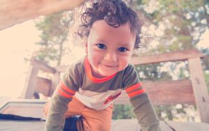 Niño con ojos grandes arrastrándose en un juego de madera en el bosque con el sol detrás