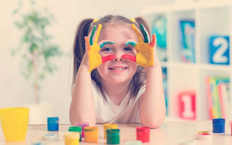 linda niña alegre mostrando sus manos pintadas de colores brillantes