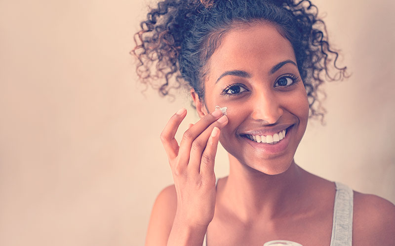 Mujer sonriente mientras se aplica una crema