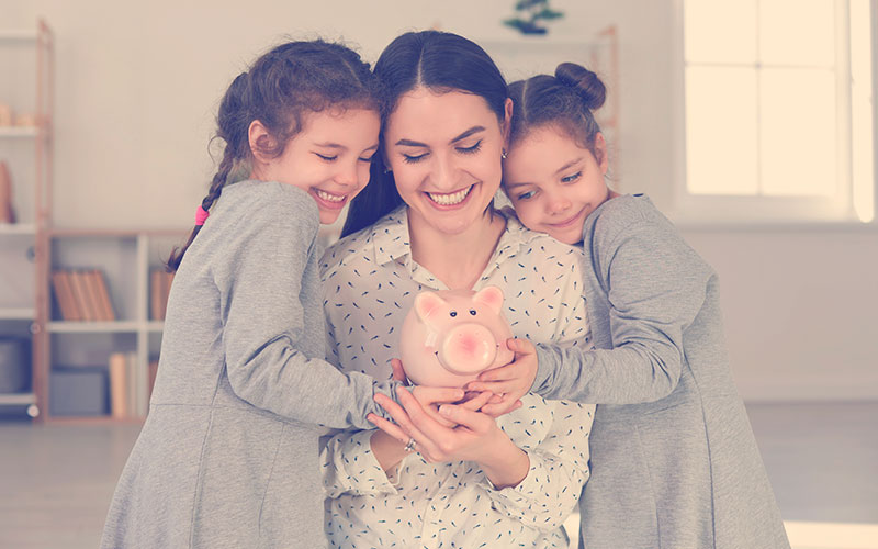 Mamá con dos de sus hijas sosteniendo un marranito para ahorrar dinero