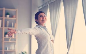 Mujer feliz recibiendo el sol desde su ventana