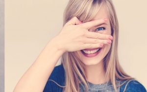 Mujer sonriendo mientras tapa uno de sus ojos