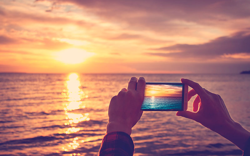 manos de mujer sosteniendo el teléfono móvil al atardecer