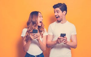 Foto de gente positiva y emocionada, hombre y mujer gritando y mirándose mientras ambos usan teléfonos móviles aislados sobre fondo amarillo