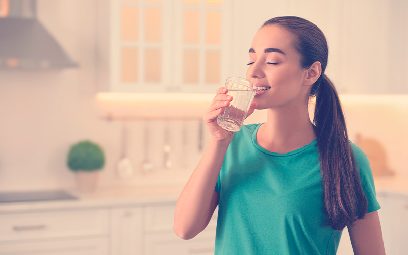 Mujer joven bebiendo agua pura de un vaso en la cocina.