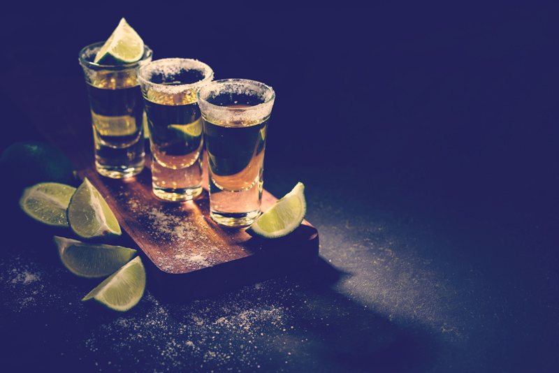 Tequila de oro mexicano con lima y sal sobre mesa de madera, enfoque selectivo.