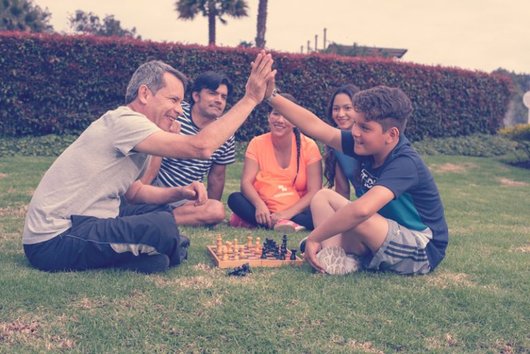 Familia de cinco integrantes sonriendo, sentados en el jardin jugando ajedrez