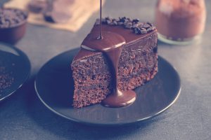 Vaciando salsa de chocolate en deliciosa tarta fresca en mesa gris