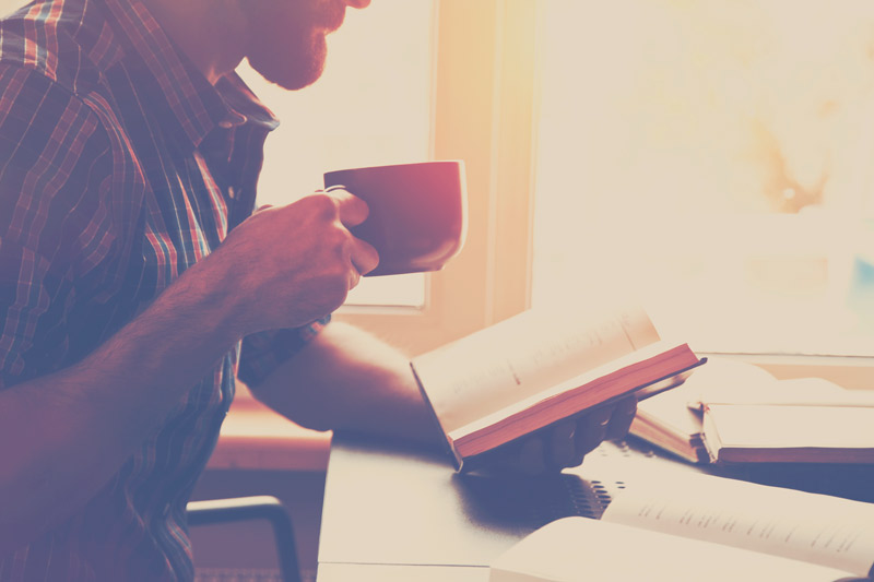 hombre barbudo leyendo libro con café o té