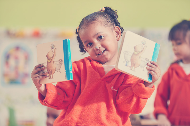 Niña pequeña en su salón de clases mostrando dos libros que le gustan