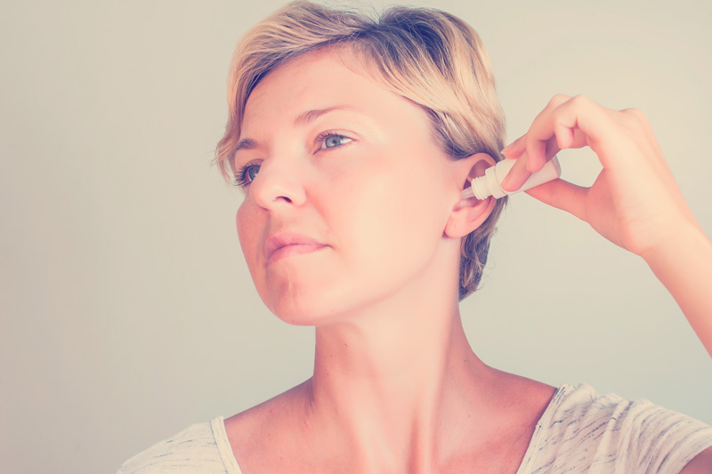 mujer que usa gotas en el oído sobre fondo gris