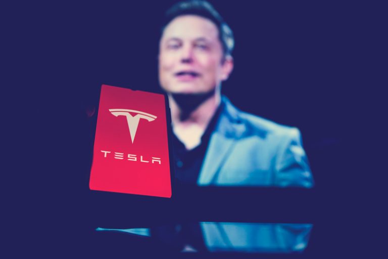 Elon Musk con celular con fondo de pantalla Tesla