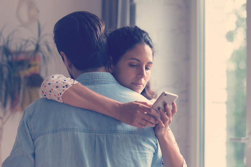 mujer abraza a un hombre mientras revisa su celular