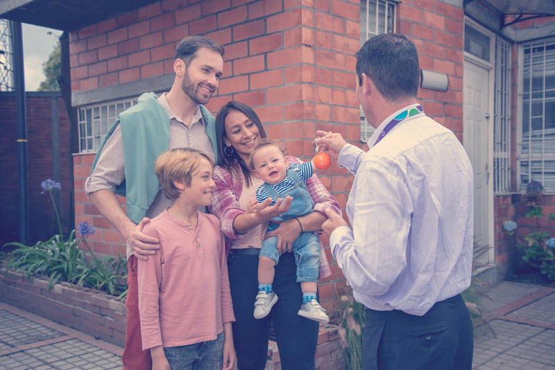 Familia de cuatro integrantes sonrientes recibiendo las llaves de su casa propia