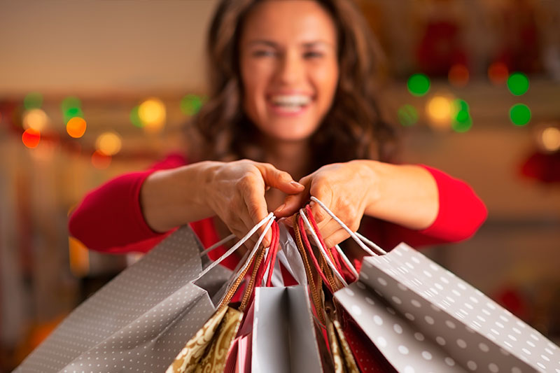 Mujer sonriente sosteniendo bolsas de compras decorativas durante la temporada de fin de año, representando la emoción de los compradores