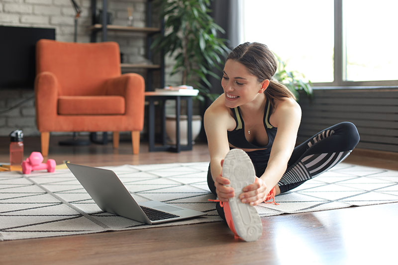 Mujer practicando una de las rutinas de ejercicio efectivas en casa usando su laptop.