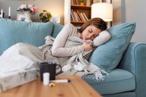 Mujer con síntomas de influenza H3N2 guardando reposo en casa con termómetro y pañuelos.