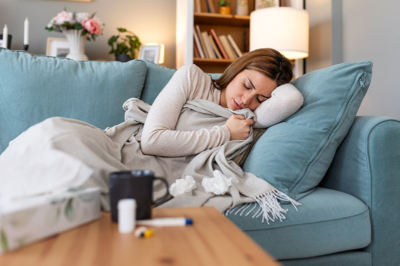 Mujer con síntomas de influenza H3N2 guardando reposo en casa con termómetro y pañuelos.