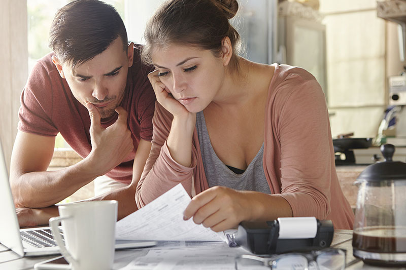 Pareja joven analizando facturas y presupuesto familiar para aprender como salir de deudas de forma efectiva.