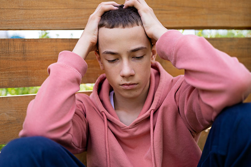 Adolescente con expresión de agobio y las manos en la cabeza, representando señales de estrés o problemas de salud mental.