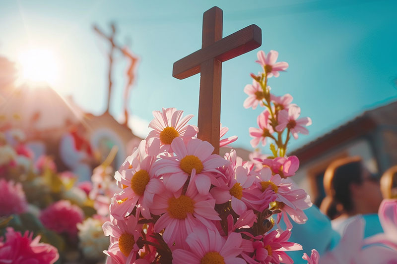 Flores rosadas adornando una cruz de madera, representando las tradiciones de Semana Santa y la Pascua en el mundo.