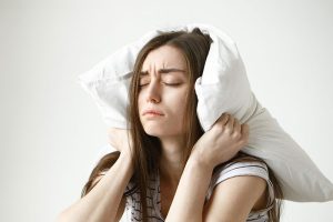 Mujer con insomnio se tapa las orejas con una almohada con expresión desesperada, ilustrando los trastornos del sueño en mujeres.