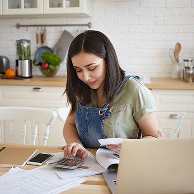 Mujer joven utilizando una calculadora y organizando facturas, siguiendo los pasos de como salir de deudas mediante un presupuesto mensual.