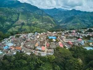 Vista aérea de un pueblo de Cundinamarca rodeado de montañas Andinas, que ilustra el contraste entre la vivienda rural vs urbana y la agricultura en Colombia bajo un cielo nublado.