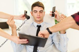 Empleado estresado rodeado de manos con teléfonos y tareas, representando la falta de desconexión laboral en Colombia.