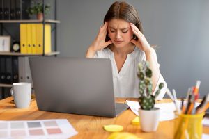 Mujer joven en una oficina tratando de manejar el estrés laboral frente a su computadora portátil.