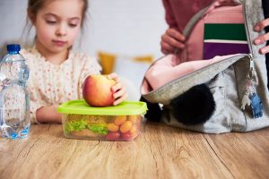 Niña preparando loncheras saludables para niños con frutas frescas y envases reutilizables para el colegio.