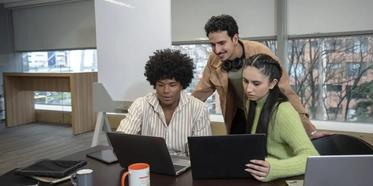 Tres colaboradores jóvenes trabajando con laptops en un entorno de aprendizaje y desarrollo profesional, representando la retención de talento mediante la formación en tecnología e IA.