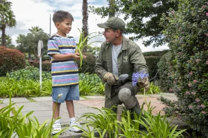 Un niño y un jardinero plantando brotes, demostrando acciones de cultura ambiental y sostenibilidad empresarial en un entorno urbano.
