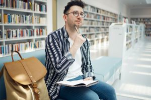 Estudiante pensando cómo elegir una carrera profesional en una biblioteca universitaria.