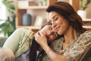 Madre relajada abrazando a su hija, representando el bienestar emocional y el autocuidado materno.